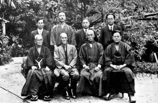 La primera reunión oficial entre los principales exponentes del kárate, en Naha el 25.10.1936, con el objetivo de difundir el arte marcial de Okinawa por toda la nación japonesa. De izquierda a derecha: Shimpan Shiroma, Tsuyoshi Chitose, Chōshin Chibana y el periodista Genwa Nakasone. De izquierda a derecha: Chōtoku Kyan, Kentsū Yabu, Chōmo Hanashiro y Chōjun Miyagi. Según fuentes recientes, la foto fue tomada unos días después (nótese que faltan los conocidos Chōki Motobu y Jūhatsu Kyoda).